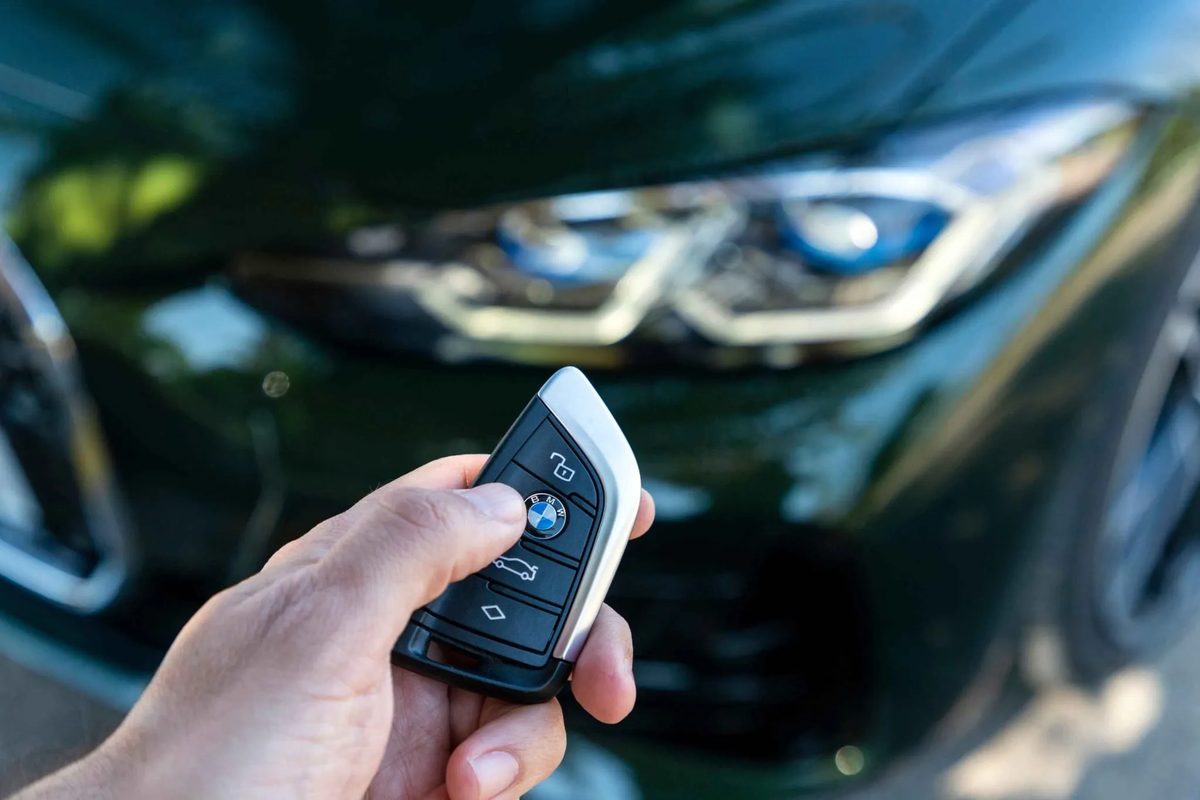 BMW-smartkey in de hand, met de BMW op de achtergrond