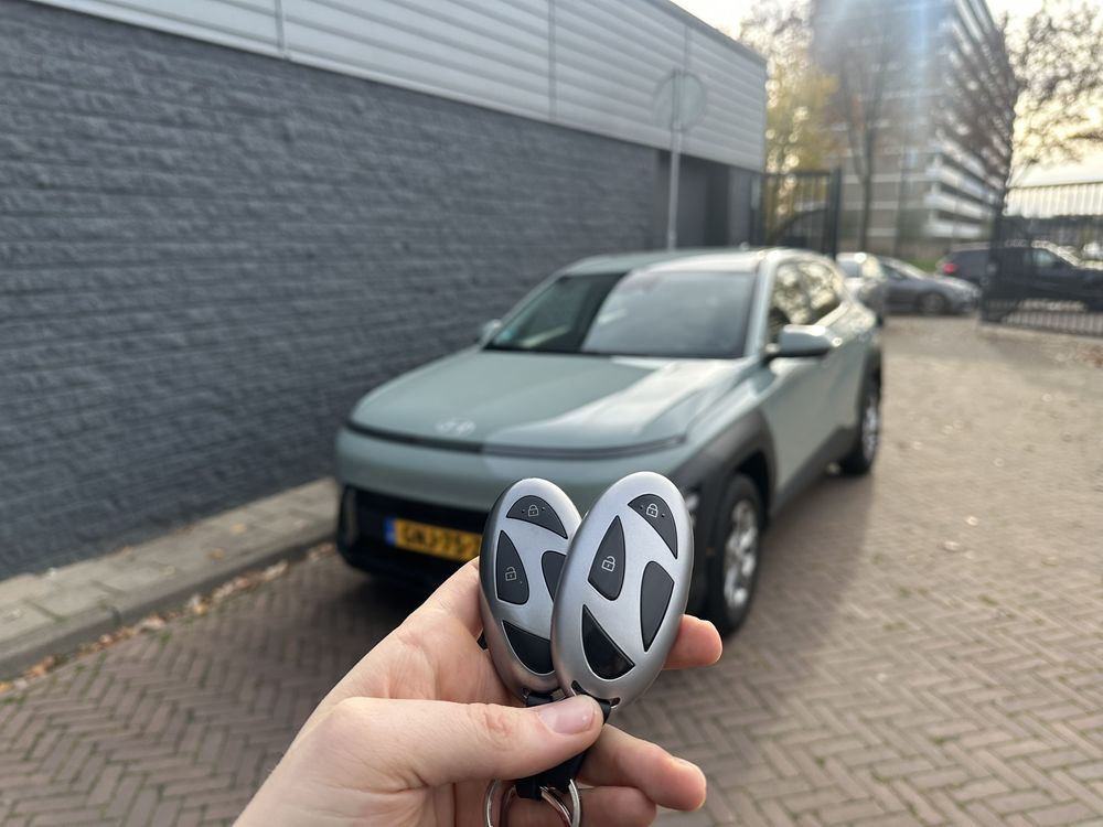 Twee Hyundai-smartkeys in de hand, met een Hyundai Kona op de achtergrond