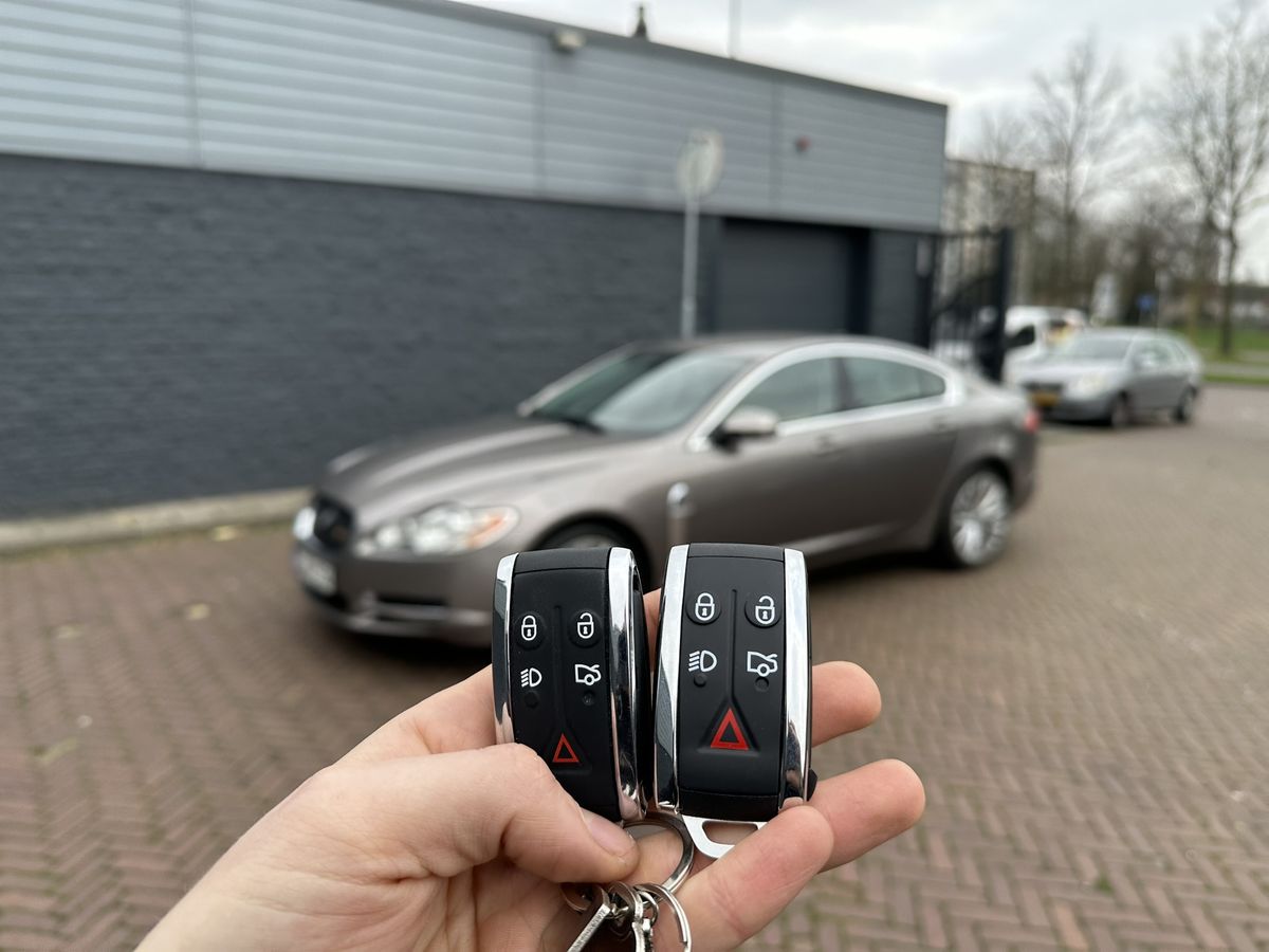 Twee Jaguar-smartkeys in de hand, met een Jaguar XF op de achtergrond