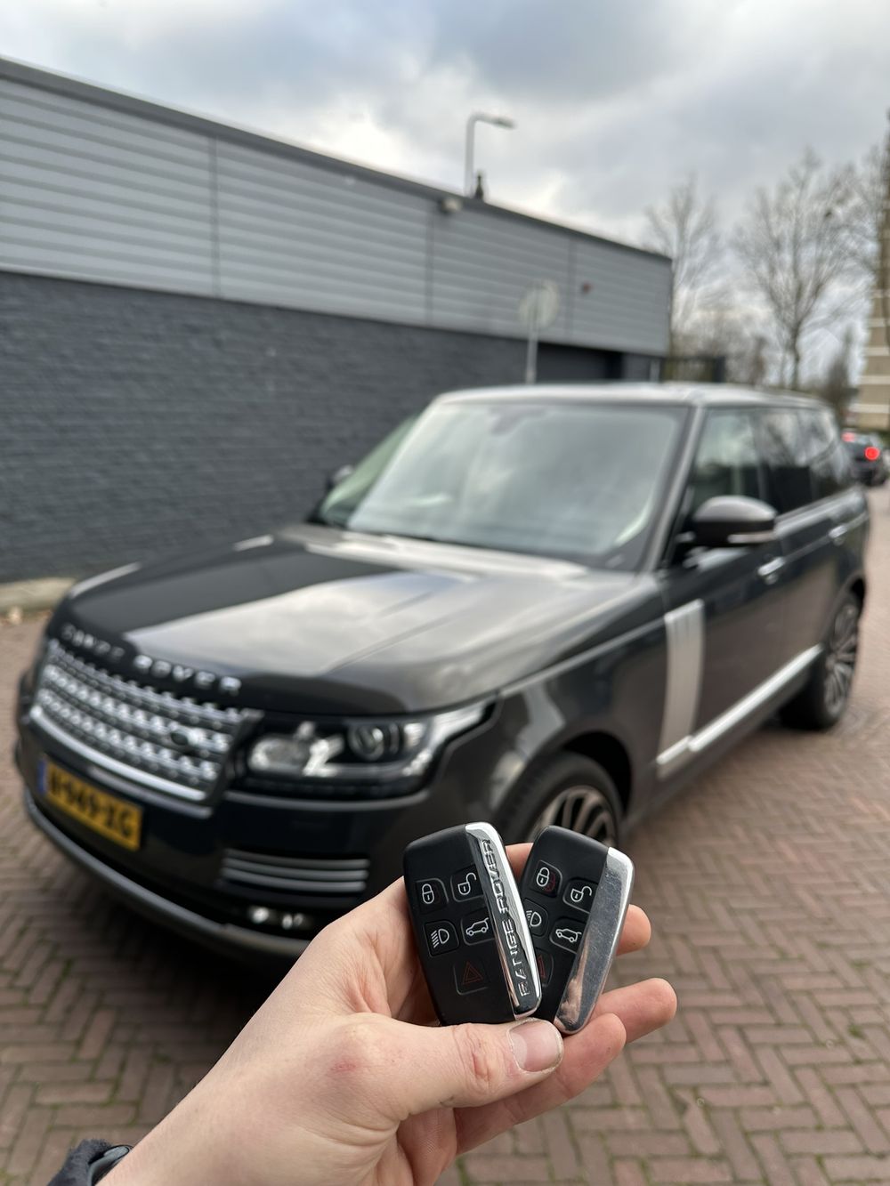 Twee Range Rover-sleutels in de hand, met de Range Rover op de achtergrond
