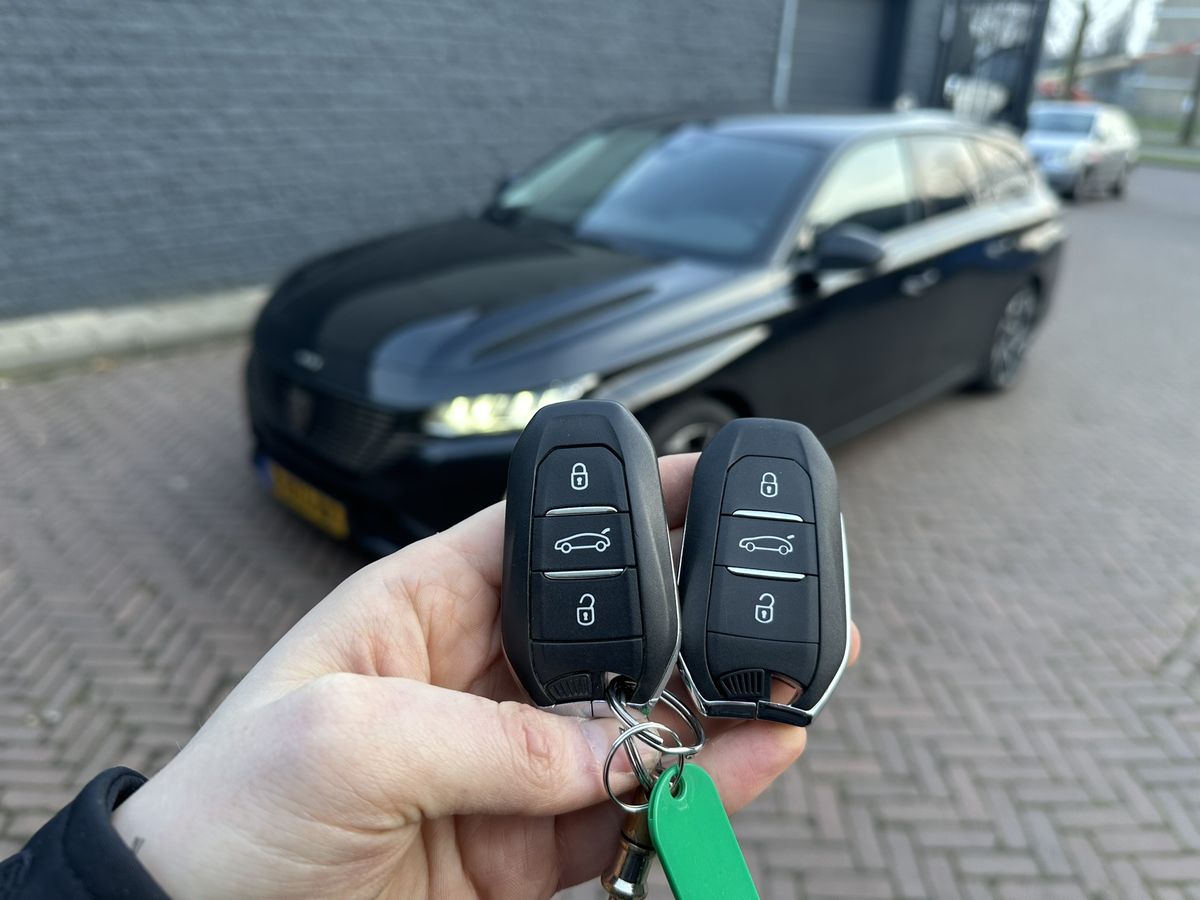 Twee Peugeot-smartkeys in de hand, met een Peugeot 508 op de achtergrond