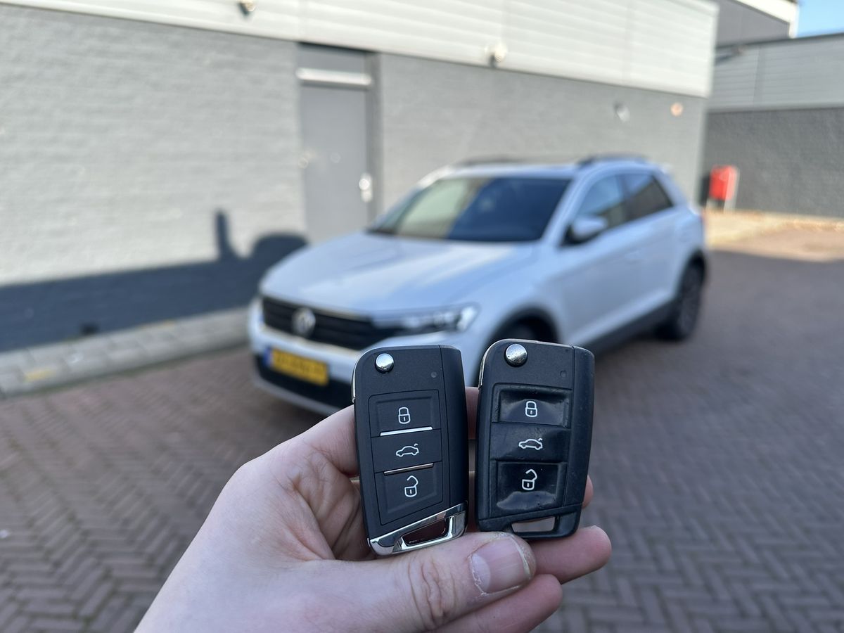 Twee Volkswagen-klapsleutels in de hand, met een witte T-Roc op de achtergrond